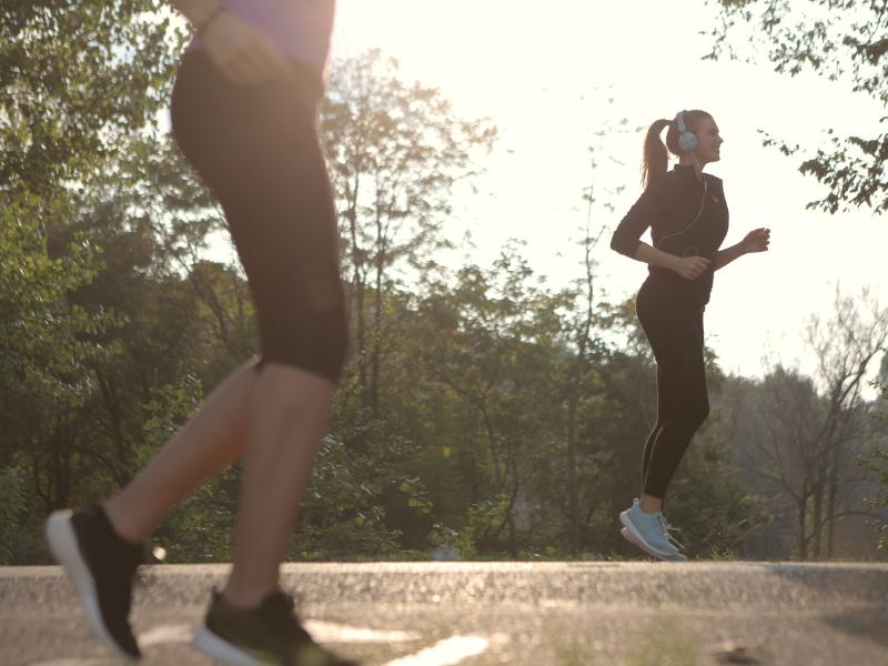 Woman, in black exercise gear and headphones, jogging with another woman in foreground shown only from waist down. Boost your attention with exercise.