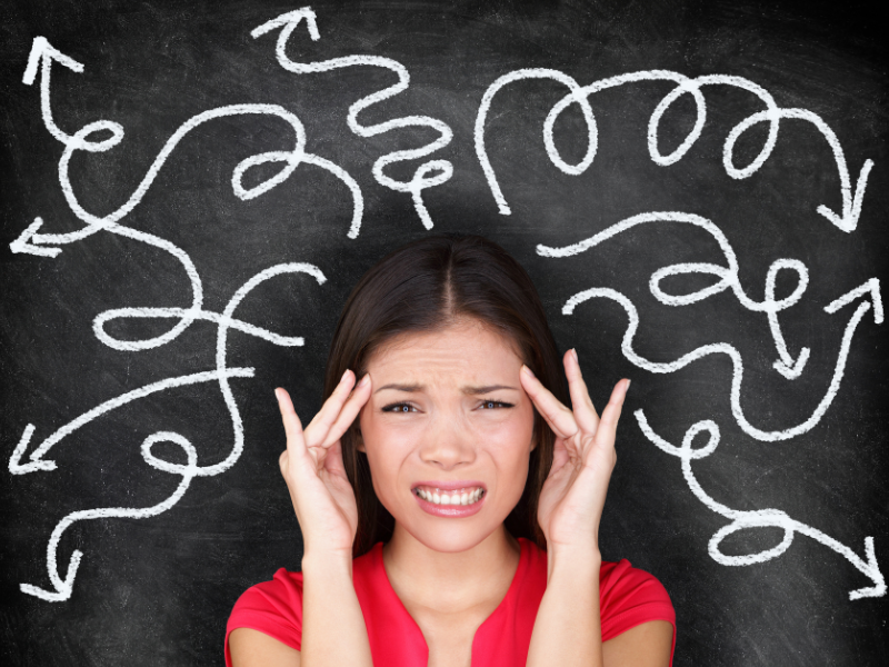 Face of confused looking woman in red top in front of blackboard with spiralled white arrows pointing in many different directions. Boost your attention with meditation exercise and sleep.