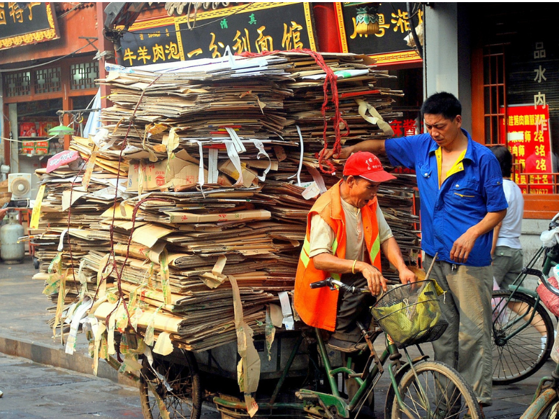 Man on bike carrying a huge pile of compacted cardboard. Low-tech solutions for sustainability.