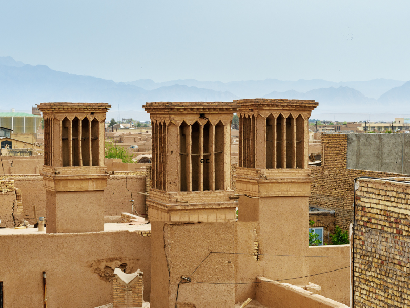 Ancient light brown windcatcher towers up above city with mountains in background. Low-technology solutions for sustainability.