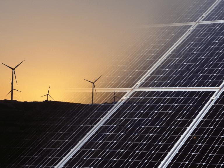 wind farms silhouetted against a hazy sunset in left upper corner, and close up of solar panels in right hand side of picture.