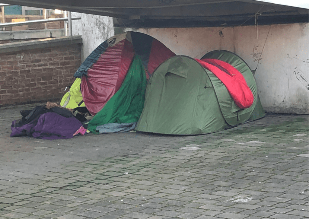 Two green and red tents side by side under a city overpass