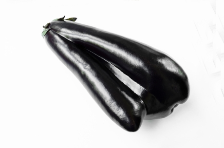 An odd-shaped black coloured eggplant with a white background