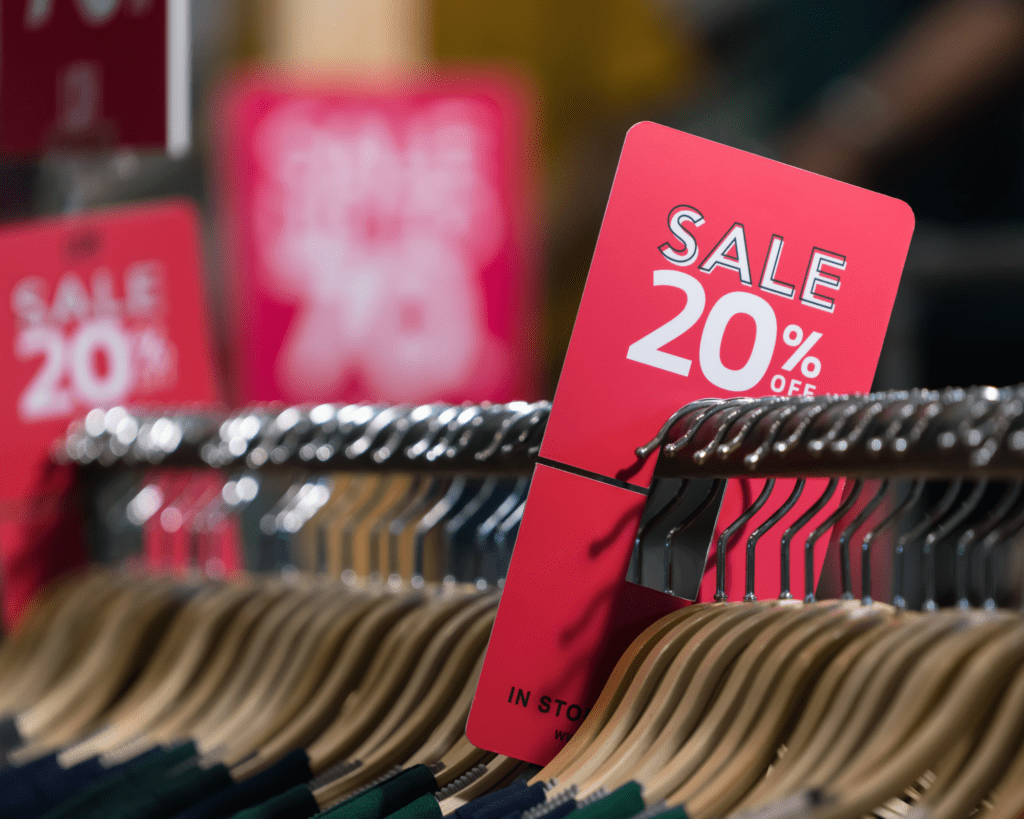 A store with a rack of clothes on coat hangers with red Sale 20% off signs 