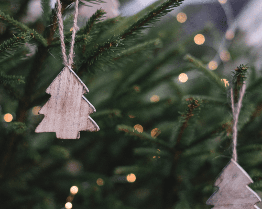 Close up of a brown wooden christmas tree decoration hanging on a green christmas tree with fairy lights