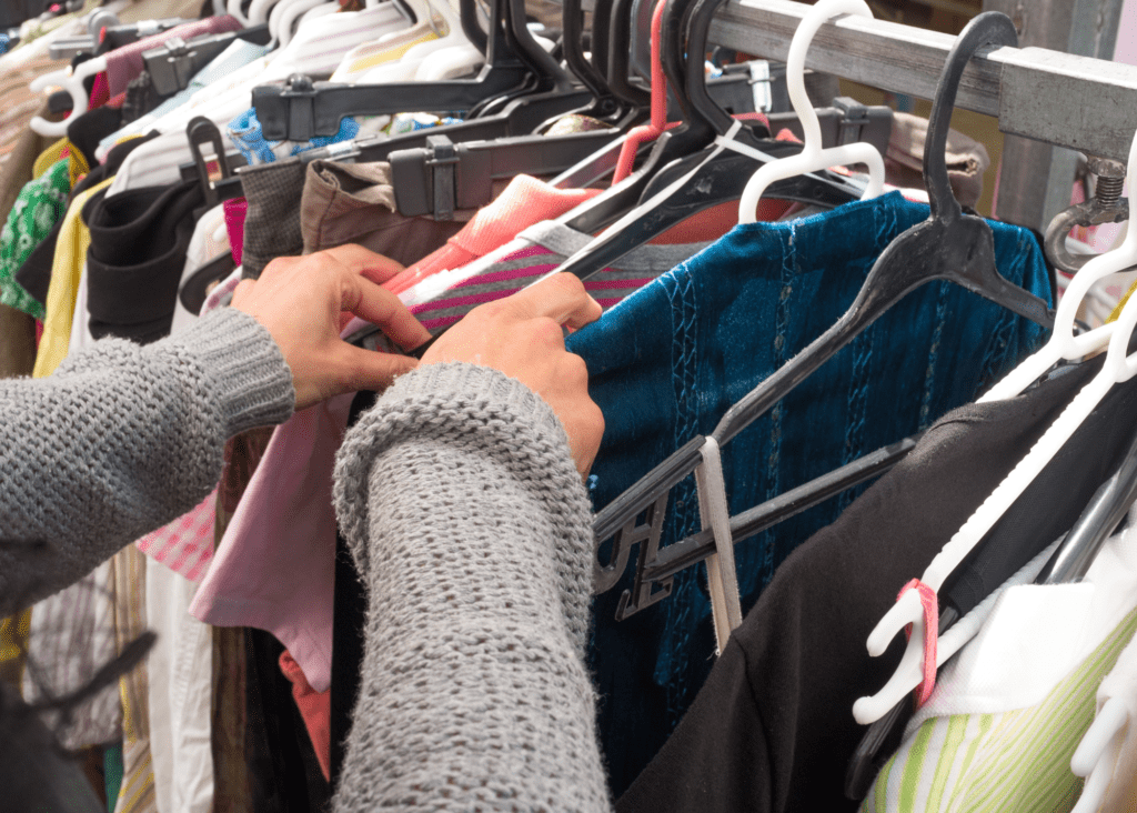 Someone's arms with grey sleeves searching through a rack of second-hand clothes