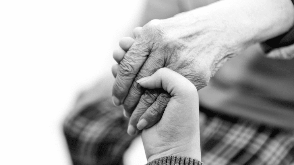 A black and white photo of a young person's hand holding an older person's hand.