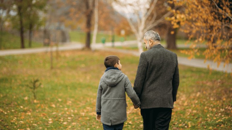 Older man walking hand in hand with boy through a park