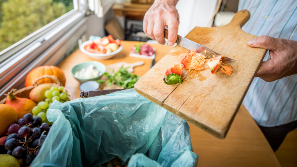 Man's hand using knife to scrape food scraps into compost bin lined with plastic bag