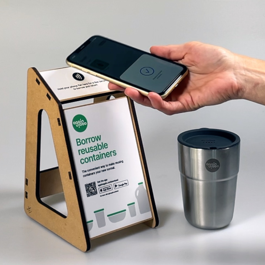 Hand holding mobile phone to tap pay next to a reusable cup