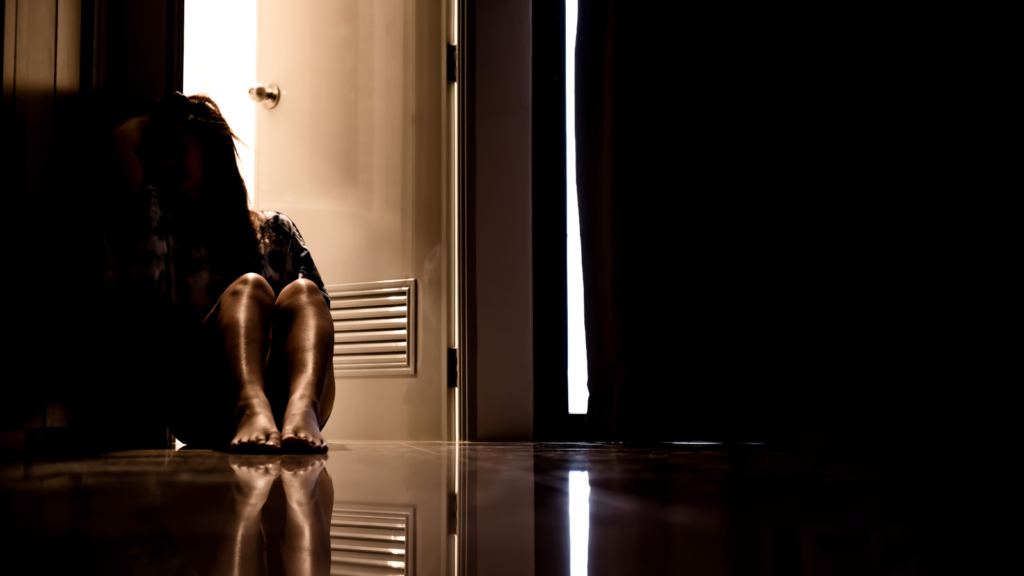 Lone woman sitting on floor in the dark next to an open door