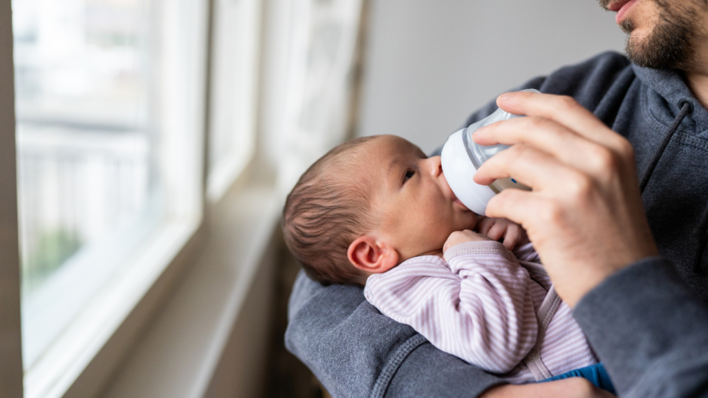 A bearded man bottle feeding a small baby