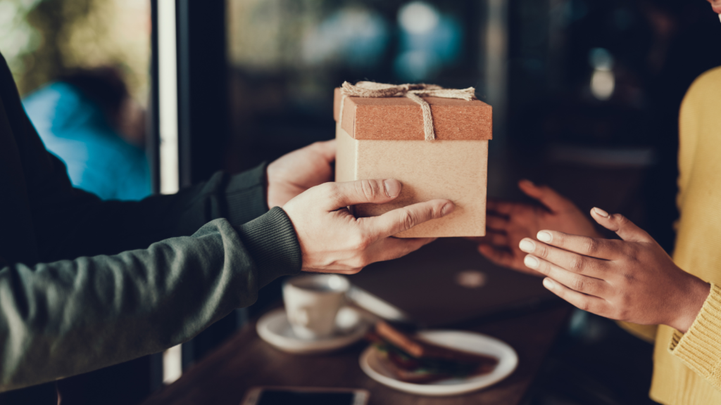 One person handing a boxed gift to another.