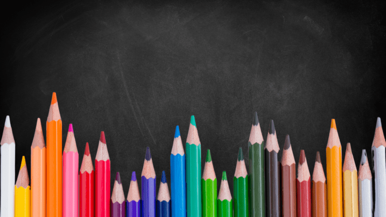 A variety of coloured pencils against a blackboard.