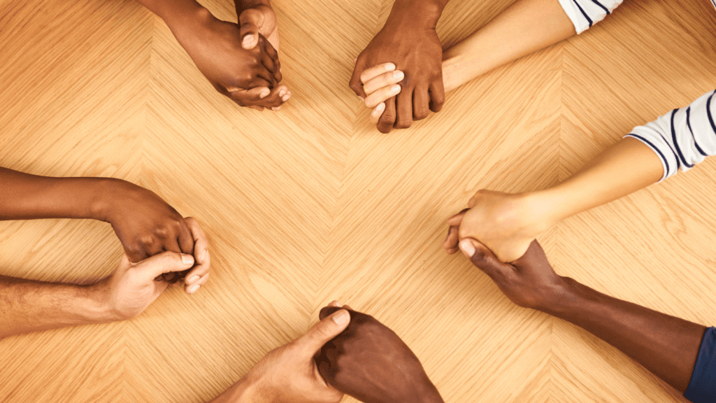 The hands of four friends holding hands over a table 