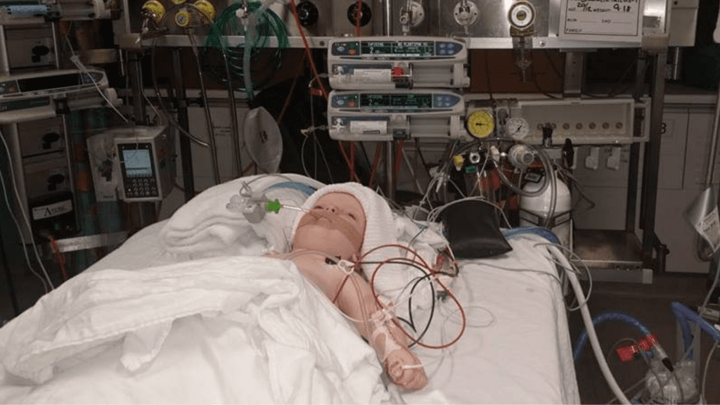 A child lying in a hospital bed, with tubes and wires