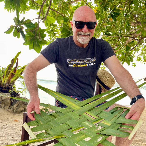 A bald man in sunglasses weaving a coconut leaf basket