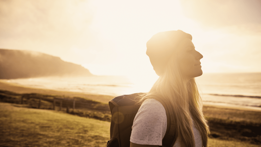 A woman on a beach, practising mindfulness, with the sun shining in the background.