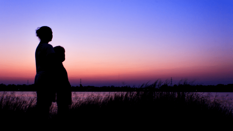 the silhouette of a mother and her child against the backdrop of the colours of a sunset