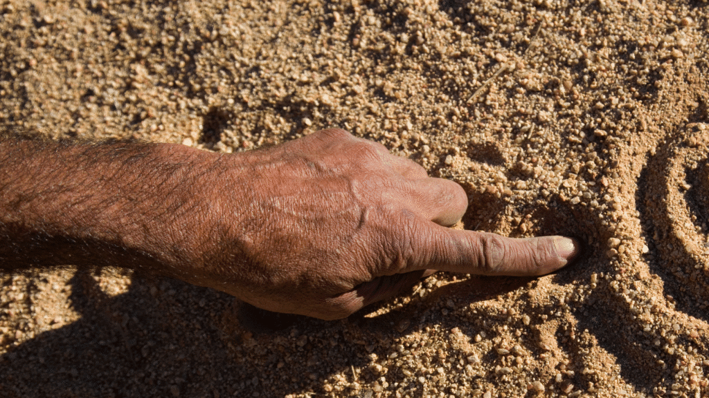 A close up of an Aboriginal man's hand drawing dreamtime stories in the dirt.